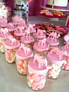 pink and white cupcakes in glass jars on a table with other dessert items