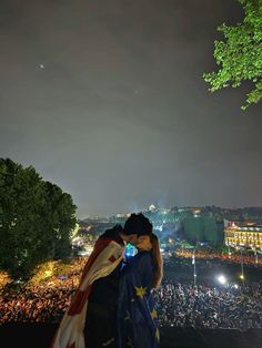 two people kissing each other in front of a large crowd at night with lights on