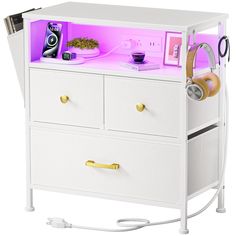 a white cabinet with two drawers and some items on it's sides, in front of a purple light