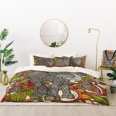 a bed with an elephant design on the comforter and pillow cases next to potted plants