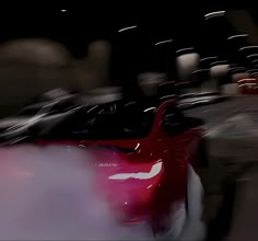 a blurry photo of a red sports car in the dark with its hood up