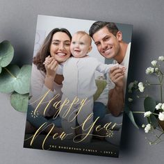 a happy new year card with a gold foil lettering and a photo of two people holding a baby