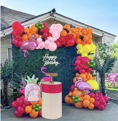 a birthday decoration with flamingos, pineapples and balloons on the side of a house