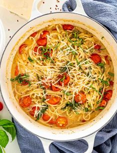 a pot filled with pasta, tomatoes and parmesan cheese on top of a blue towel