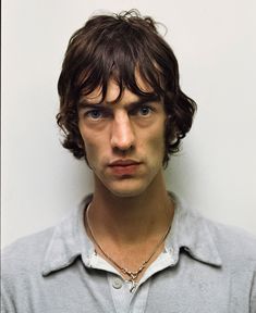 a man with long hair and blue eyes is looking at the camera while wearing a gray shirt