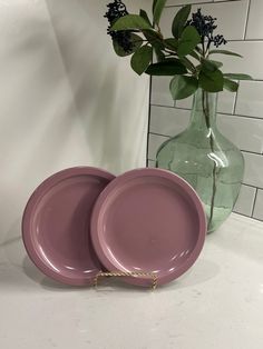 two pink plates sitting on top of a counter next to a vase