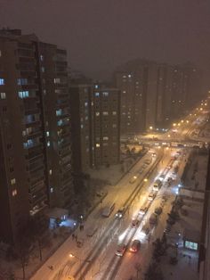 an aerial view of a city street at night with snow on the ground and buildings