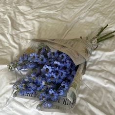 a bouquet of blue flowers is wrapped in plastic on a white sheeted bed spread