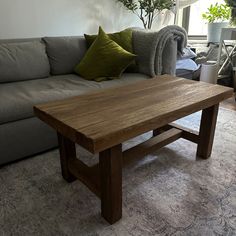 a wooden table sitting in front of a gray couch with green pillows on top of it