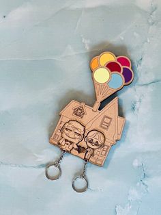 a wooden keychain with two cartoon characters on it and some balloons in the air