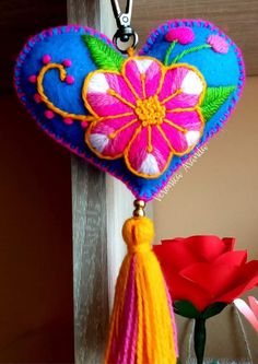 a colorful heart shaped decoration hanging from a hook on a wooden door with flowers in the background