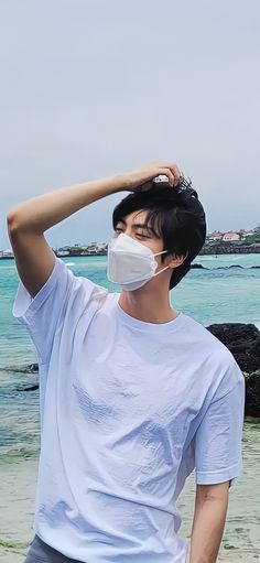 a man wearing a face mask standing on the beach with his hair in front of him