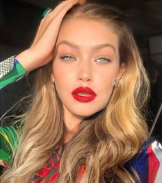 a woman with long blonde hair and bright red lipstick wearing green bracelets, holding her hand on her head