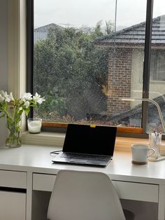 a laptop computer sitting on top of a white desk next to a window covered in rain