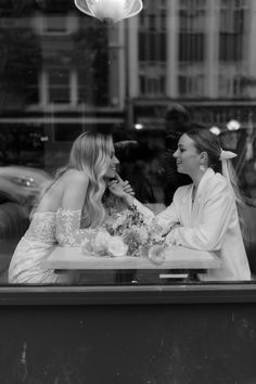 two women sitting at a table in front of a store window talking to each other