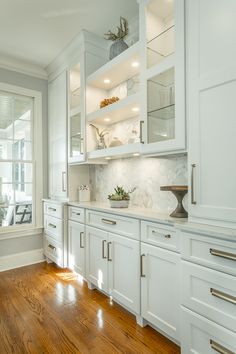 a kitchen with white cabinets and wood flooring next to a large window in the corner