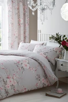 a white bed with pink flowers on it and a chandelier hanging from the ceiling