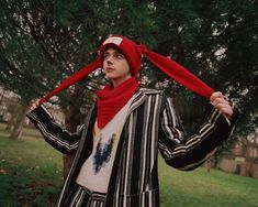 a man wearing a red hat and striped jacket is holding his scarf over his head