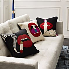 three pillows on a white couch in front of a blue vase with red lips and lipstick