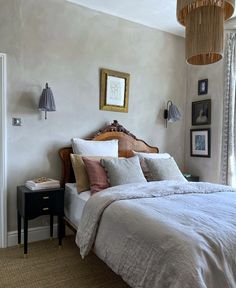 a bed with white sheets and pillows in a bedroom next to a window, framed pictures on the wall