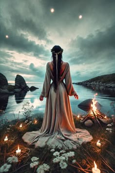 a woman with long hair standing in front of a body of water surrounded by lit candles