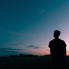 a man standing in the middle of a field at sunset