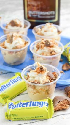 some desserts are in plastic cups on a blue napkin and next to a bottle of butterfinger