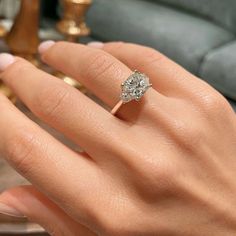 a woman's hand with a diamond ring on top of her finger, in front of a couch