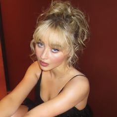 a woman in a black dress is sitting on a red chair and posing for the camera