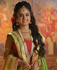 a woman in a green and yellow sari with pearls on her head, smiling at the camera