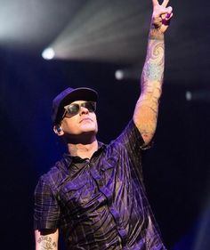 a man with tattoos on his arm giving the peace sign while standing in front of a stage