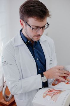 Felipe é um homem branco, com cabelos e barba curtos e loiro escuro. Na foto ele está de jaleco médico, e está lendo um livro que segura em suas mãos. Dr Andre, Branding, Skin