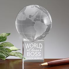 a glass globe on a wooden table with a pen and plant in the foreground