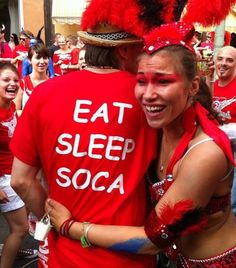 a man and woman in red shirts hugging each other while people watch from the street