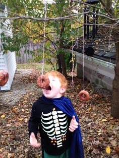 a young boy wearing a skeleton costume and holding a donut in his mouth while standing next to a tree