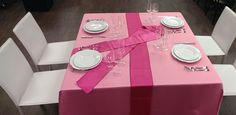 the table is set with white plates and silverware, pink satin ribbon on it