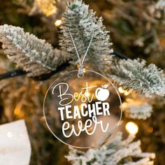 a glass ornament that says best teacher ever hanging from a christmas tree with lights in the background