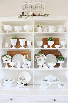 a white china cabinet filled with dishes and plates on top of wooden shelves next to a birdcage