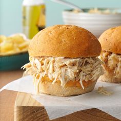 two pulled pork sandwiches sitting on top of a wooden table next to a bowl of macaroni and cheese