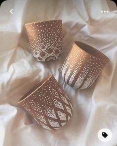 three brown and white cups sitting on top of a bed next to eachother