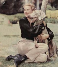 a woman sitting on the ground holding a dog in her lap and smiling at the camera