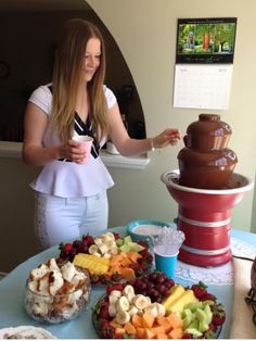 a woman standing in front of a chocolate fountain with fruit and other foods on it