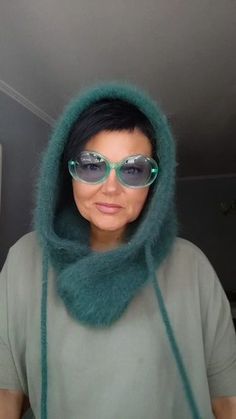 a woman wearing sunglasses and a green fur hood over her head is looking at the camera