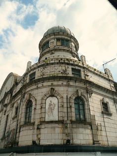 an old building with a clock on the side of it's face in front of a cloudy blue sky