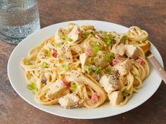 a white plate topped with pasta covered in chicken and veggies next to a glass of water