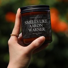 a hand holding a jar of smells like aaron warnner scented candle in front of an orange tree