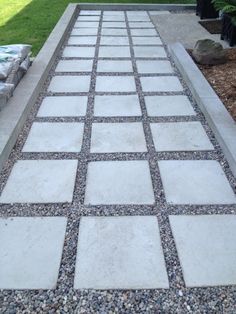 an outdoor walkway made out of concrete blocks and gravel with grass in the back ground