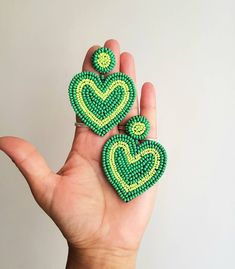 a hand holding two green and yellow beaded heart shaped earrings