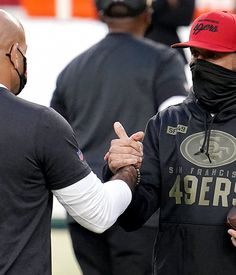 two men in black jackets and red hats are shaking hands with each other on the sidelines