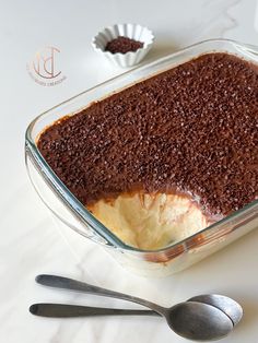 a cake in a glass dish with two spoons next to it